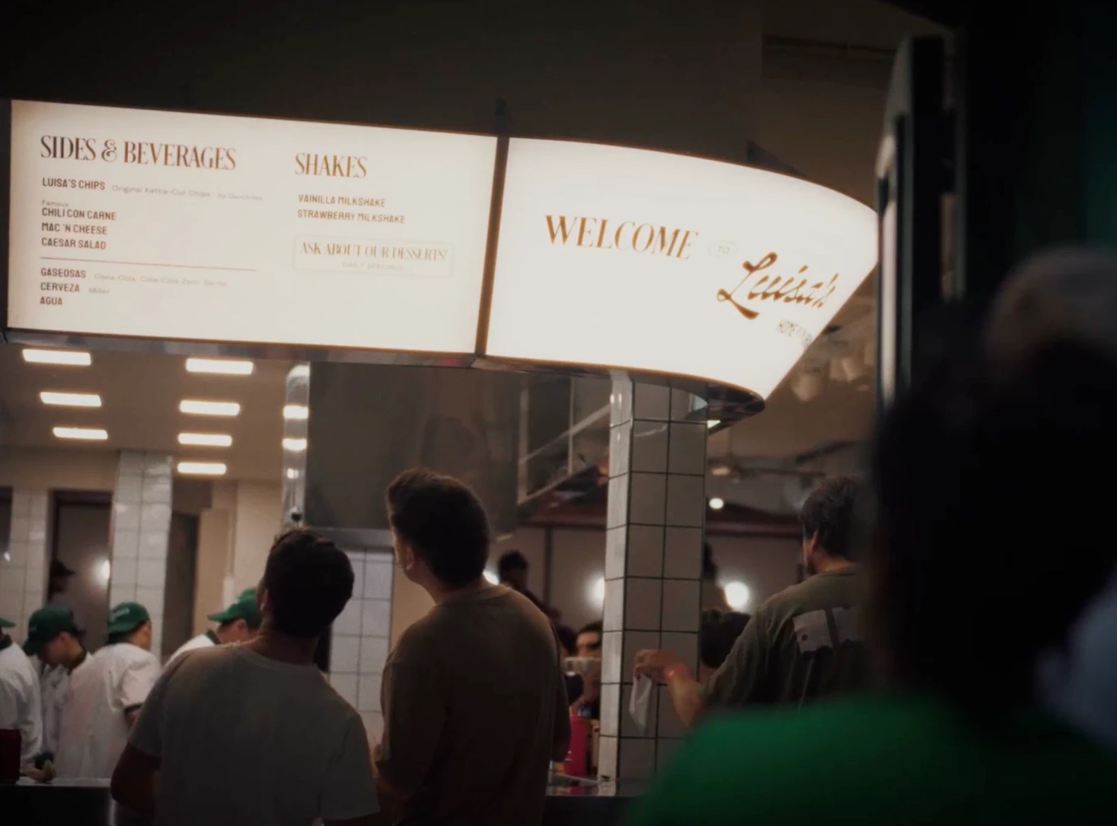 Clientes frente a los carteles iluminados del menú de Luisa's